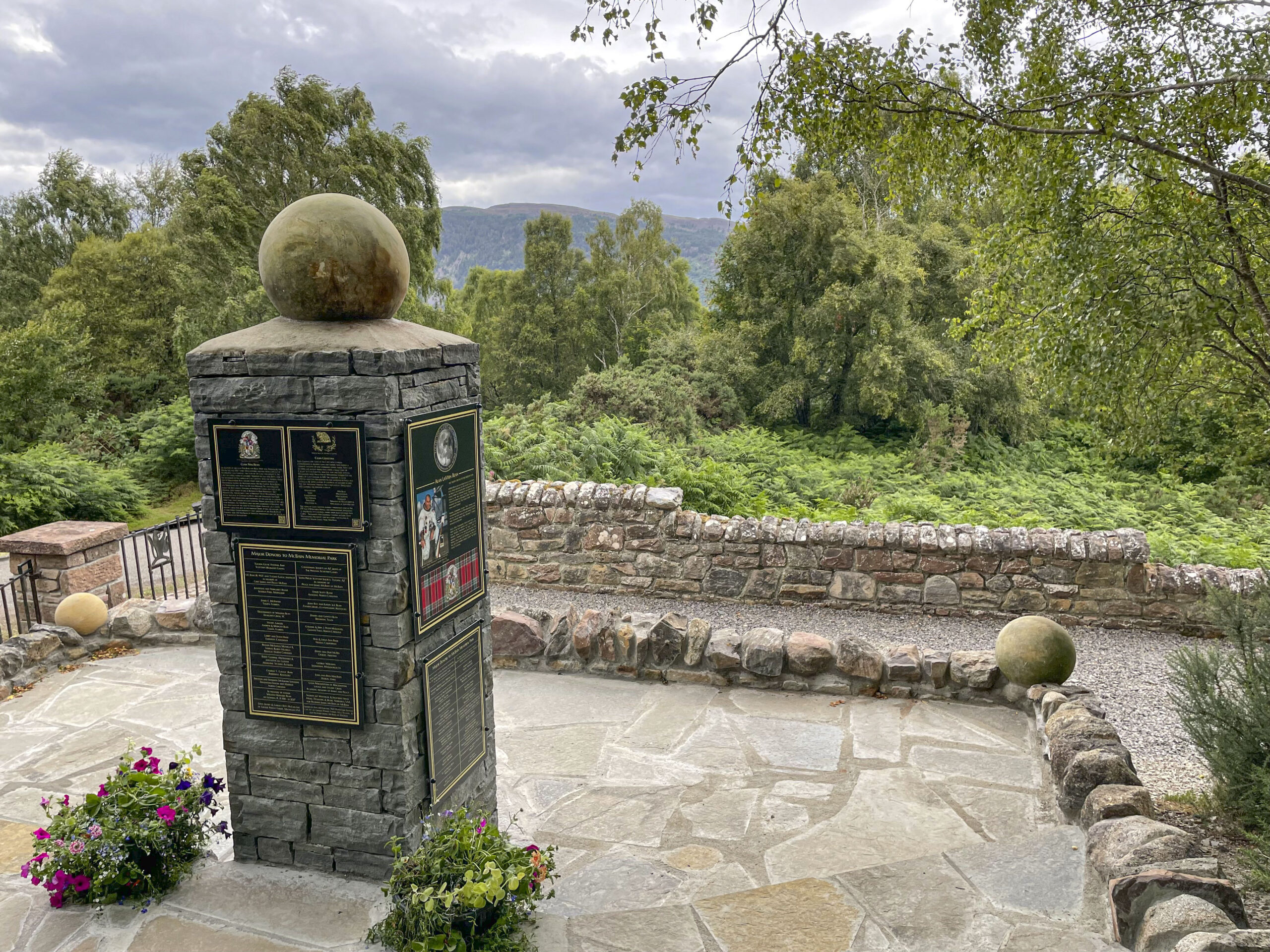 The Alan Bean Memorial: a dry-stone pillar topped with a stone moon, carrying the clan plaques, on a flagstone terrace in the McBain Memorial Park